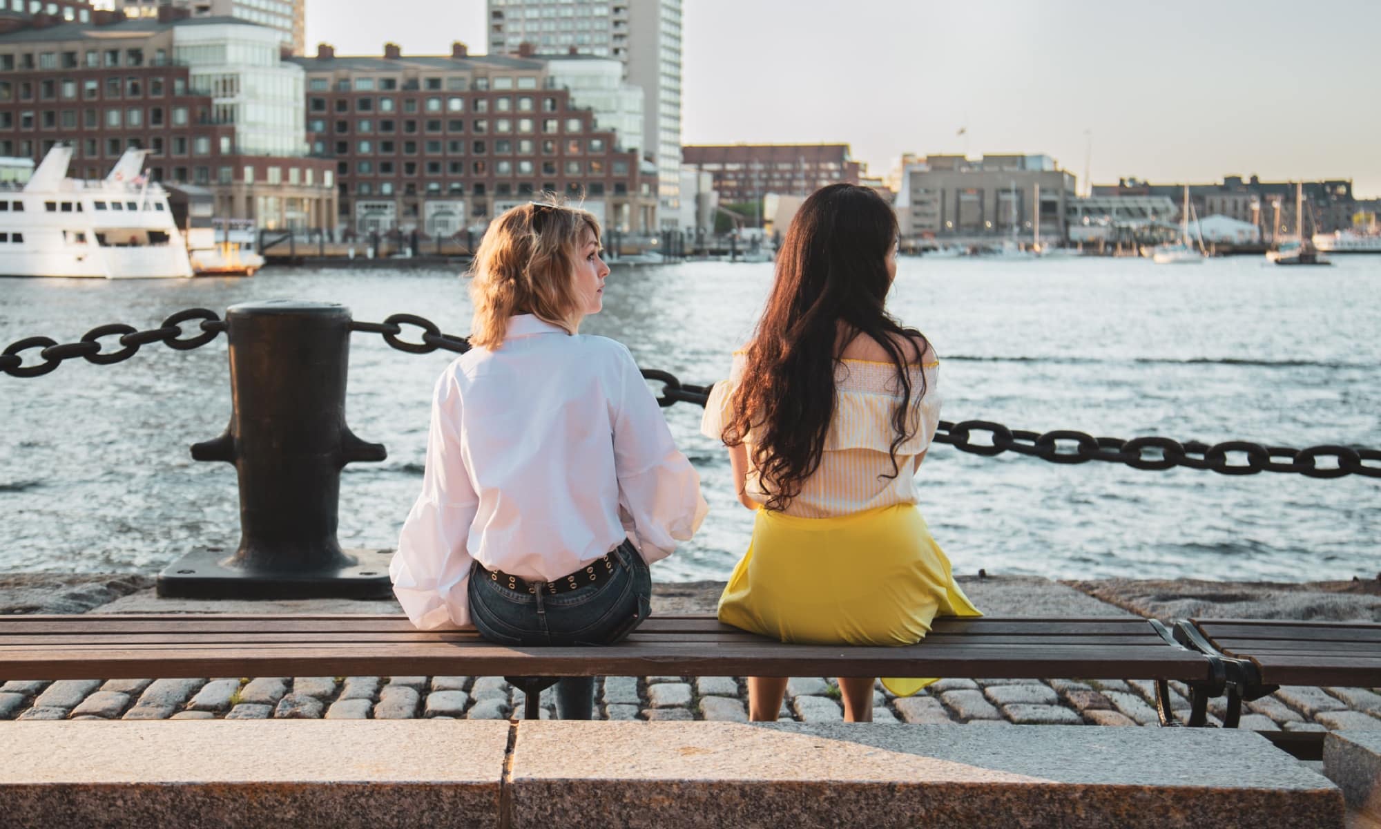 Two young women sit by the waterside in downtown Boston